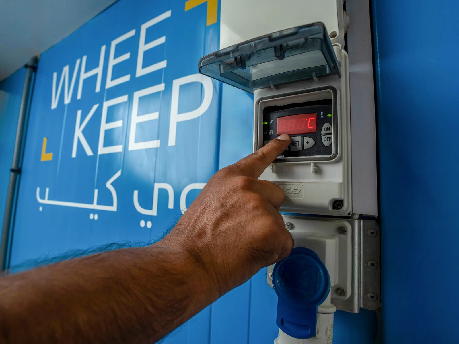 A hand setting the temperature controller on a WheeKeep air-conditioned unit