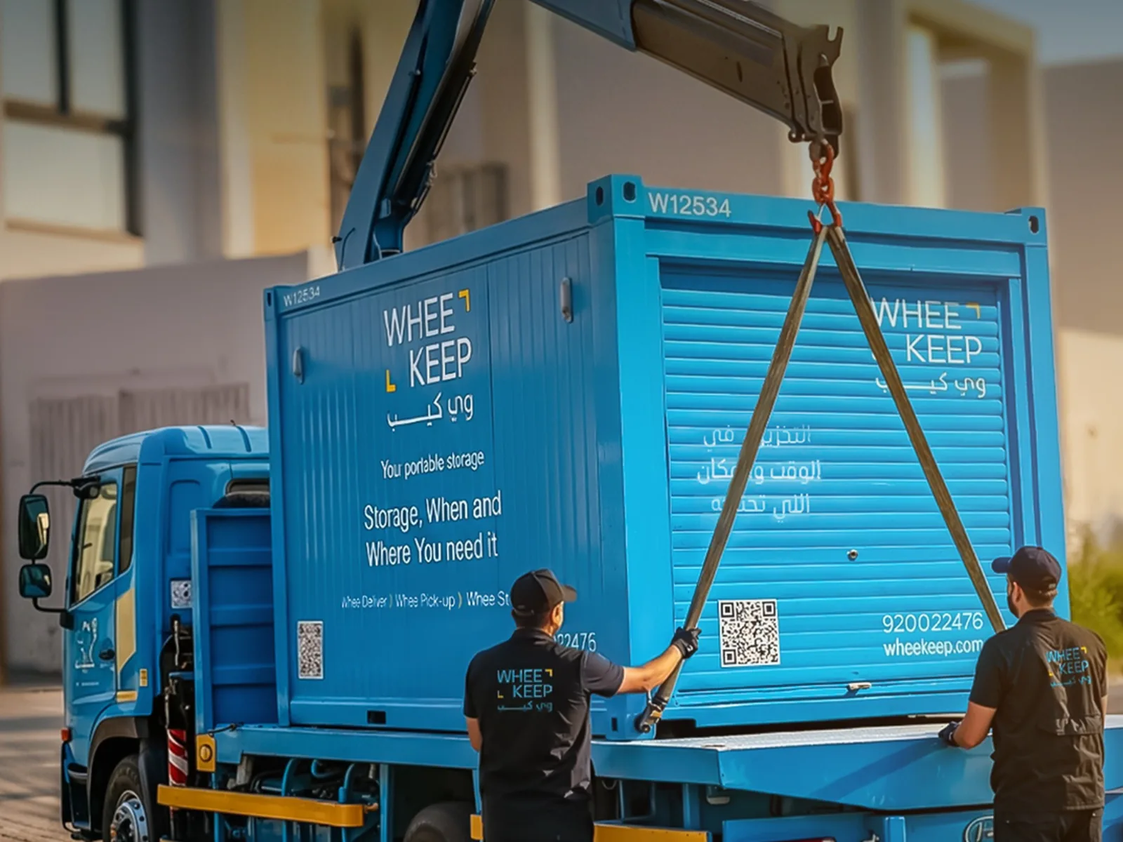 A WheeKeep truck lifting a roll-up-door storage unit by crane